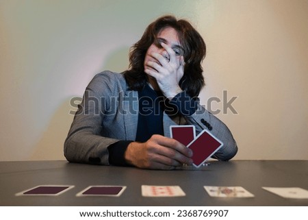 Man in a suit playing poker - card game and holding his mouth while holding his playing cards. Surprised, sad, gambling addiction concept. Royalty-Free Stock Photo #2368769907