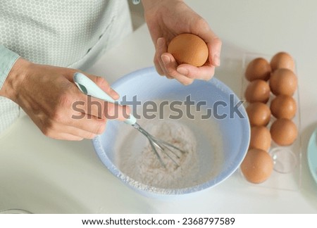 Close up of a woman's hands whipping eggs for making dough on the white desk in the kitchen. Homemade cooking