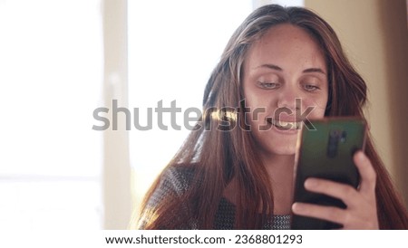 pretty girl looking at smartphone near the window. internet social network concept. girl makes online purchases on a smartphone near the window at home sun. girl reading news on a smartphone