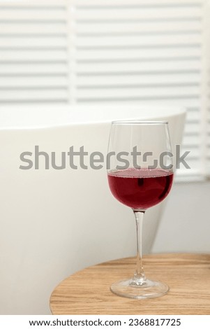 Glass of red wine on wooden table in bathroom