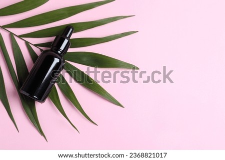 Bottle with cosmetic oil and green leaf on pink background, top view. Space for text