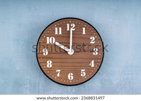 Brown Wooden clock placed in middle of blue cement wall.