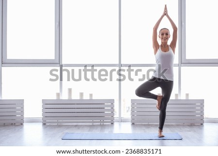 Beautiful girl in sportswear is looking at camera and smiling while doing yoga
