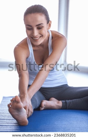 Beautiful girl in sportswear is smiling while stretching on yoga mat in sports hall