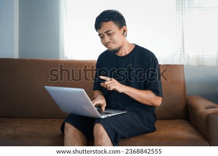 People And Technology. Portrait Of Smiling Asian Man Holding And  Tablet Sitting On Couch Indoors In Living Room. 
