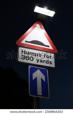 Hump road sign with text "Humps for 360 yards" with one way sign taken at night, sign illuminated by lamp