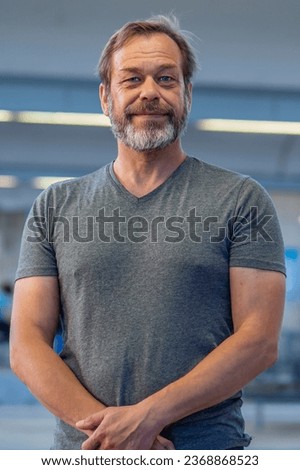 portrait of happy man 50-55 years old with beard in gray T-shirt on blurred background of railway station, vertical photo. Concept:buyer or actor, loader or military pensioner. Royalty-Free Stock Photo #2368868523