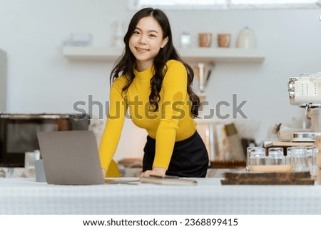 Beautiful Asian woman smiling happily relaxing using technology of laptop computer Take notes Drink a relaxing hot drink while sitting on the table in your room at home.