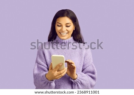 Happy woman uses mobile phone for online shopping, chatting, messaging or browsing social networks. Beautiful joyful woman enjoys capabilities of modern mobile phone on pastel purple background. Royalty-Free Stock Photo #2368911001