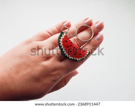 The hand holds a key with a keychain in the form of a slice on a white background. Bead colorful key chain in a female hand