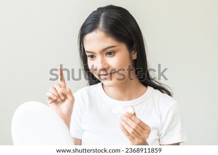 Ophthalmology care, eye sight, vision concept, happy asian young woman, female holding and putting soft contact lenses with finger on face from box case, looking in mirror at home. Medicine and health Royalty-Free Stock Photo #2368911859