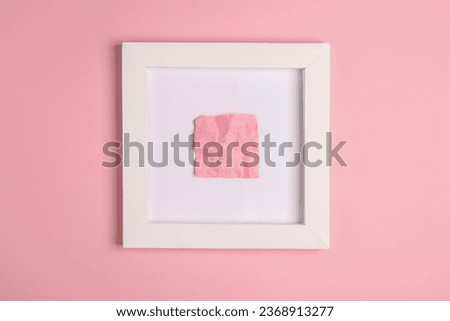 Crumpled memo paper in white square frame, pink background. Aesthetic minimal still life. Conceptual photo. Modern art. Top view
