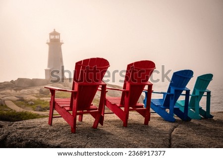 Four Adirondack chairs facing Peggy's Cove Lighthouse during foggy sunset evening, Nova Scotia, Canada. Photo taken in September 2023.
