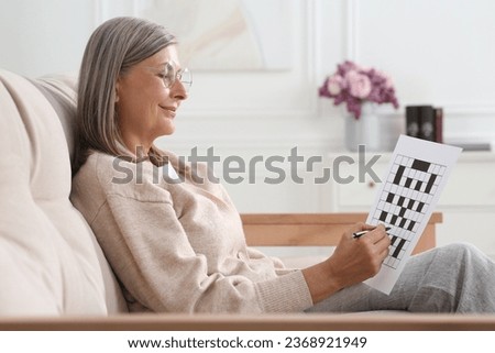 Senior woman solving crossword on sofa at home Royalty-Free Stock Photo #2368921949