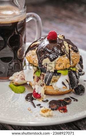 Sweet Burger on wooden background. food. Sugared burger with chocolate, cream, cookies, marshmallows, whipped cream, berries. Cola in a beer mug in the background. Freak burger. Close-up