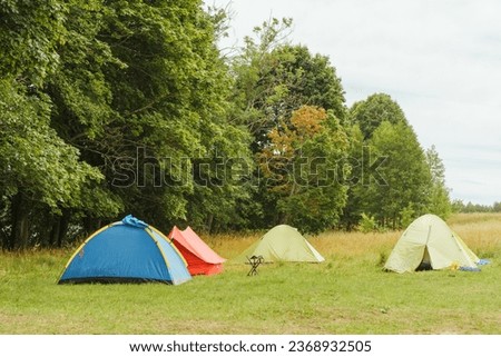 Picture of four tents of different colors set up amidst untouched nature, standing on meadow near lush greenery with nobody around. Blue, red and green shelthers ready for unforgettable camping.