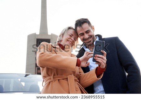 Couple using a smartphone to check social media outside the cabrio. They laugh while using the phone.