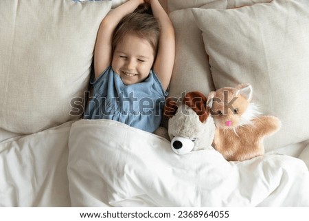 Top view of cute little preschooler girl lying cuddling with favorite fluffy toy waking up in cozy home bed, funny small kid stretch in comfortable bedroom after healthy sleep, good morning concept