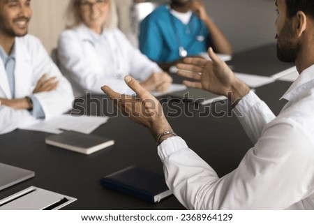 Young male doctor talking to diverse team of cheerful positive colleagues. Medical practitioners meeting for collaboration, discussing successful job cases, healthcare issues at conference table Royalty-Free Stock Photo #2368964129