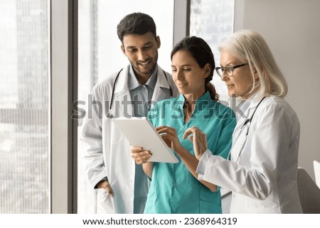 Diverse team of doctors meeting at tablet computer, using medical online service, communication, discussing application, patient test electronic results, using technology for effective teamwork