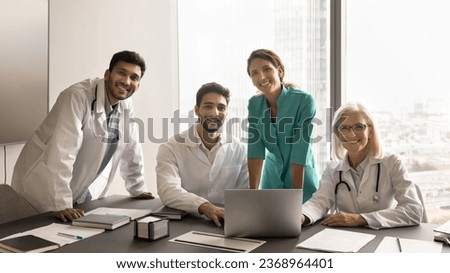 Diverse team of different aged doctors meeting at computer, looking at camera with toothy smile, posing for group professional portrait. Medical colleagues enjoying collaboration, teamwork Royalty-Free Stock Photo #2368964401