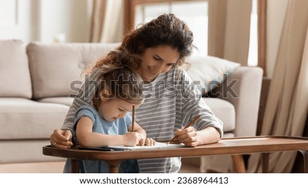 Caring young mother relax in living room drawing with cute little preschooler daughter, loving millennial mom or nanny have fun painting with colorful pencils, involved in activity with small girl
