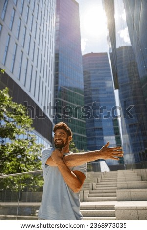 Smiling sporty man doing stretch on modern city skyscrapers background. Healthy lifestyle concept