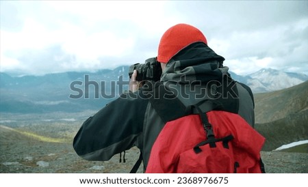 Traveler takes pictures with camera of mountain landscape with clouds. Clip. Rear view of man with backpack photographing mountain landscape. Autumn mountain landscape with traveler and camera