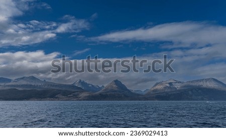A beautiful mountain range of the Andes against a background of blue sky and white clouds. View from the Beagle Canal. Ripples on the water. Argentina. Tierra del Fuego Archipelago.