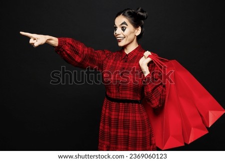Young woman with Halloween makeup face art mask wearing clown costume red dress hold shopping package bags isolated on plain black background studio. Scary holiday party concept sale buy day concept