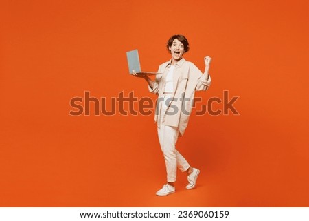 Full body side view young happy caucasian woman she wears beige shirt casual clothes hold use work on laptop pc computer do winner gesture isolated on plain orange red background. Lifestyle concept