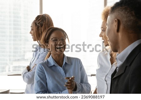Close up overjoyed African American businesswoman chatting with colleague during break, standing in office, excited employees coworkers having fun together, enjoying pleasant conversation