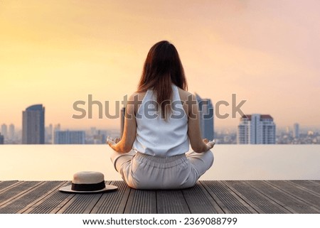 Back of woman relaxingly practicing meditation at the swimming pool rooftop with view of urban skyline building to attain happiness from inner peace wisdom Royalty-Free Stock Photo #2369088799