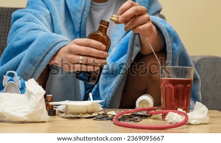 A man with a cold covered with a blanket surrounded by medicines Royalty-Free Stock Photo #2369095667