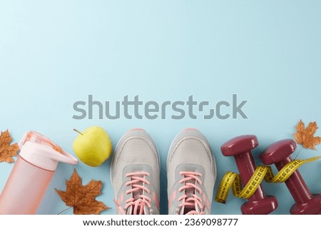 Autumn fitness transition idea. Top view photo of dumbbells, fresh apple, tape measure, stylish shoes, bottle, dry maple leaves on light blue background with advertising area