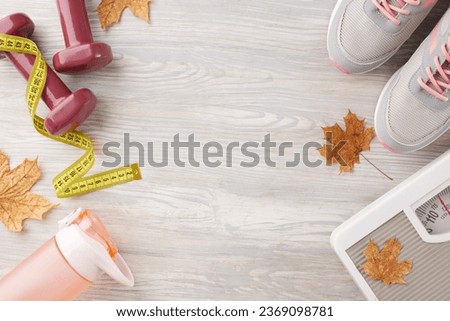 Fall season physique transformation. Top view photo of dumbbells, floor scales, tape measure, trendy shoes, bottle, dry maple leaves on light wooden background with advertising zone