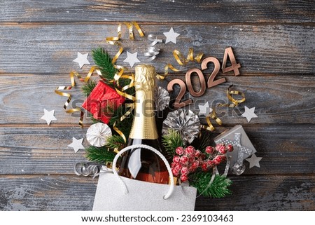 2024 New Year composition. New year holidays card with shopping bag with bottle of сhampagne, festive decorations. Gifts, present, festive New Year 2024 background