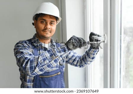 Indian Workman in overalls installing or adjusting plastic windows in the living room at home.