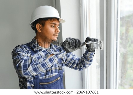 Indian Workman in overalls installing or adjusting plastic windows in the living room at home.