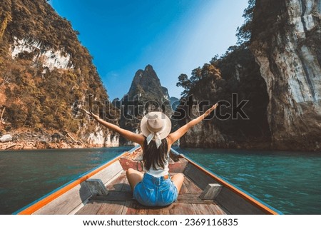 Travel summer vacation concept, Happy solo traveler asian woman with hat relax and sightseeing on Thai longtail boat in Ratchaprapha Dam at Khao Sok National Park, Surat Thani, Thailand Royalty-Free Stock Photo #2369116835