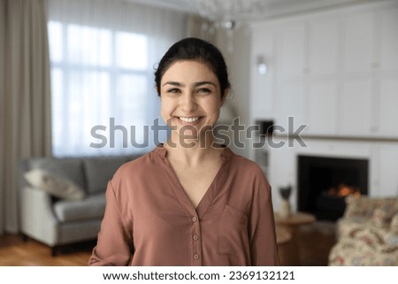 Head shot portrait positive Indian woman standing in modern living room at home, happy beautiful young female with healthy toothy smile and perfect skin looking at camera, posing for profile picture