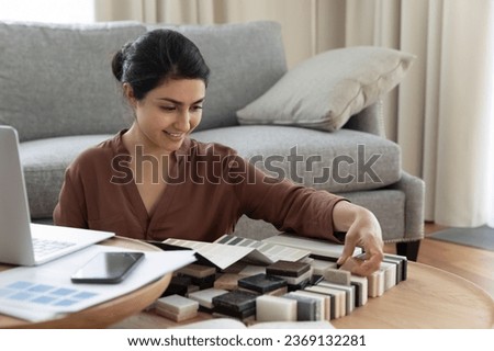 Smiling Indian woman customer choosing tile and wall paint colors from samples catalogue, young female homeowner preparing for house renovation, interior designer working on project at home Royalty-Free Stock Photo #2369132281