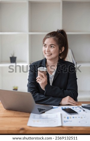 Photo of positive Asian businesswoman holds a cup of coffee imagines plan holiday in office.