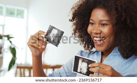 Smiling Black African American Expecting mother in curly hair showing ultrasound scan photos. Pregnancy concept.