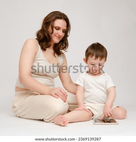 Happy baby with mother looking into digital tablet on studio white background. Portrait of a smiling child with mom and playing on the tablet. Kid about two years old (one year nine months)