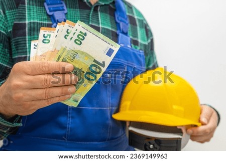 Wages in the euro area for manual workers, builders and specialists in finishing works, a specialist with a construction helmet holding a file of money in his hand Royalty-Free Stock Photo #2369149963