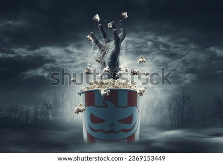 Scary zombie hand coming out of a popcorn bucket: horror movies and Halloween concept Royalty-Free Stock Photo #2369153449