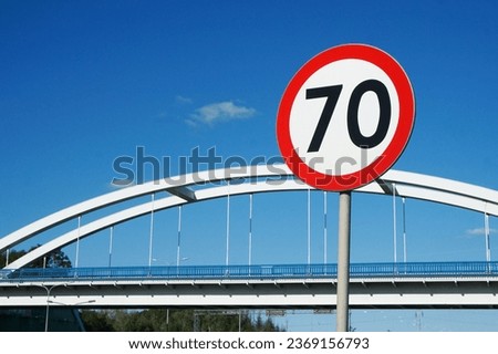 Road bridge with blue sky in the background. Road sign speed limit. 70 kmph maximum speed. Curvy construction bridge architecture. Arch bridge isolated on blue sky