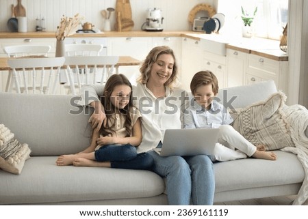 Smiling mother and cute kids sitting on cozy couch with laptop, look at device screen, smile, spend weekend time at home, having fun watching cartoons or family movie, browse internet use application