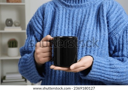 Woman holding black mug at home, closeup. Mockup for design